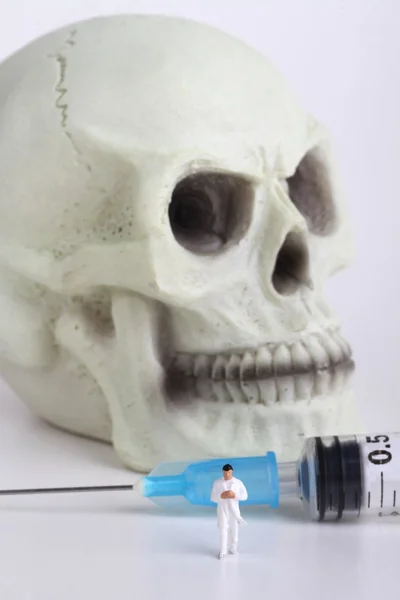 Cráneo humano, miniatura de un médico y jeringa —  Fotos de Stock