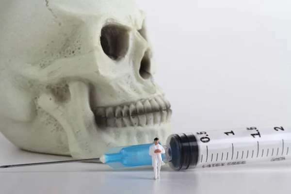 Menselijke schedel, miniatuur van een arts en spuiten — Stockfoto