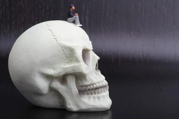 Miniature figurines of depressed people sitting on a skull — Stock Photo, Image