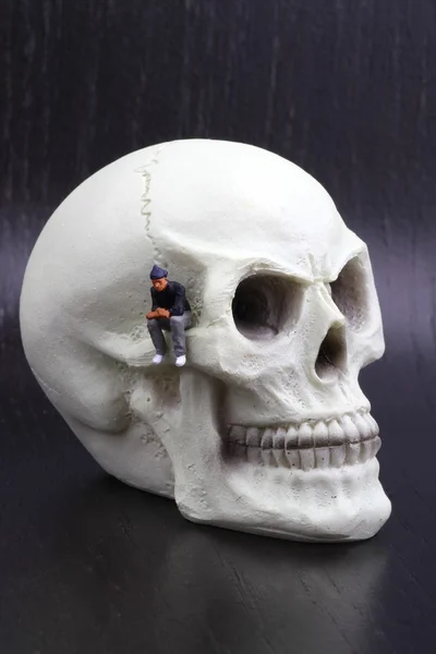Мініатюрні статуетки депресивних людей, що сидять на черепі — стокове фото
