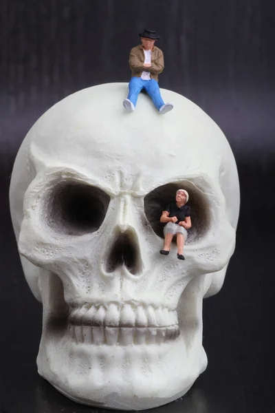 Miniature figurines of depressed people sitting on a skull — Stock Photo, Image