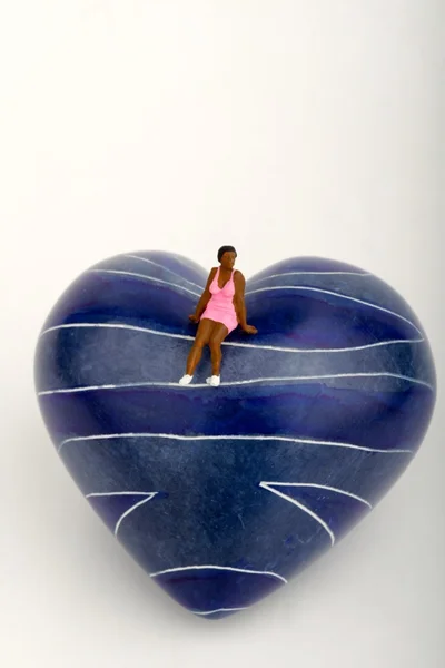 Mulher solitária em miniatura sentada em um coração azul — Fotografia de Stock
