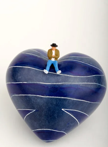 Miniaturowe samotny człowiek siedzi na szczycie kamienia w kształcie serca — Zdjęcie stockowe