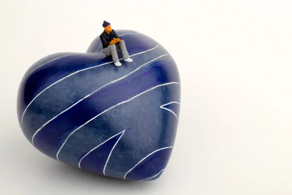 Миниатюра одинокого человека, сидящего на вершине камня в форме сердца — стоковое фото