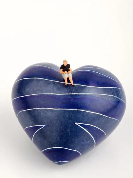 Lonely woman miniature sitting on a blue heart — Stock Photo, Image