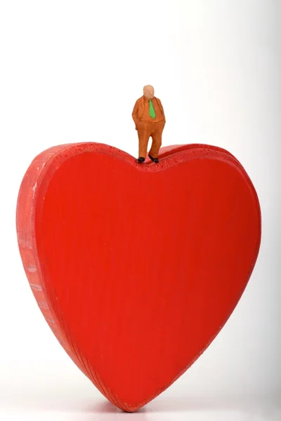 Miniatura de um homem solitário com terno de negócios em pé sobre um coração vermelho — Fotografia de Stock