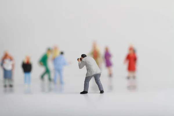 Miniature of a street photographer taking pictures of strangers walking on ta white background — Stock Photo, Image