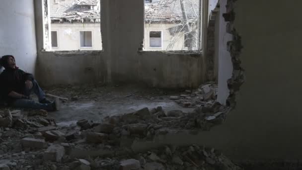 Hooded depressed young man sitting in an abandoned building — Stock Video