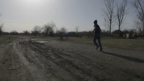 Hooded jongeman joggen in de natuur en het springen over een plas — Stockvideo