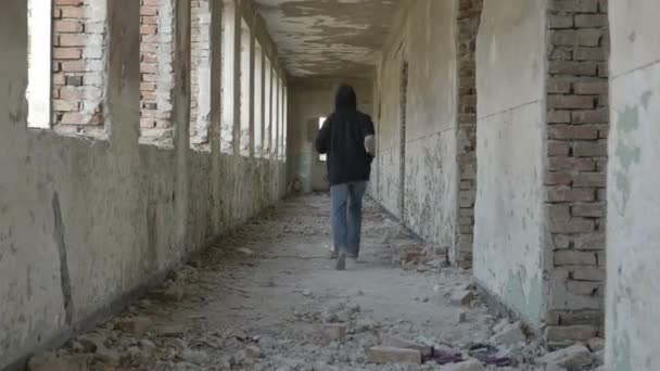 Молодой человек в капюшоне бежит в заброшенном здании — стоковое видео