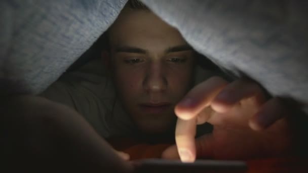 Aantrekkelijke jonge man browsen van social media op een slimme telefoon in bed — Stockvideo