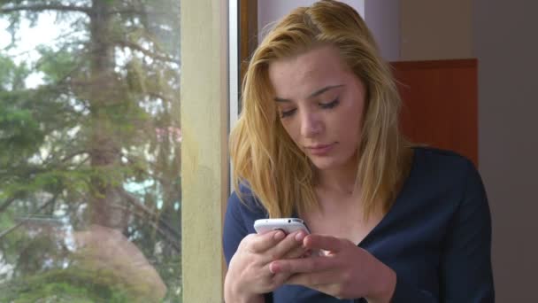 Vonzó fiatal nő textil egy okostelefon, az ablakon — Stock videók
