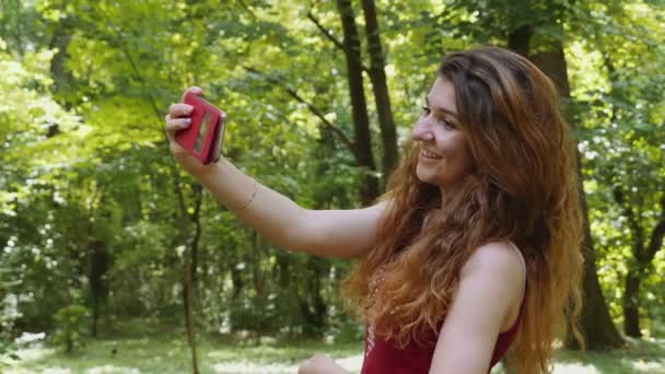 Mujer joven feliz tomando selfie con el teléfono inteligente en el parque — Vídeo de stock