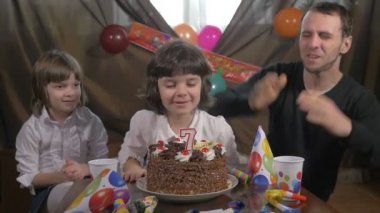 Genç güzel kız mumlar bir doğum gününde kız babası ve ikiz kardeşi, yavaş hareket ile pasta üfleme.