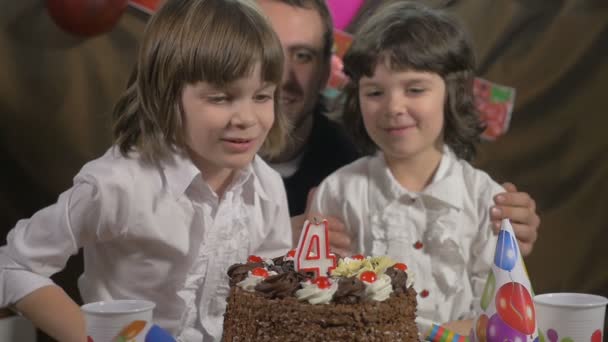 Young beautiful girl blowing candles on a birthday cake with her father and twin sister, slow motion — Stock Video