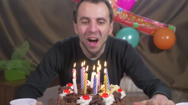 Jovem homem bonito soprando velas em um bolo de aniversário — Vídeo de Stock