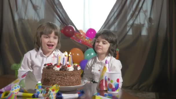 Mooi meisje blazen kaarsen op een verjaardag cake met haar tweelingzus — Stockvideo