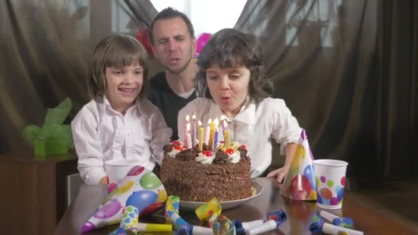 Young beautiful girl blowing candles on a birthday cake with her father and twin sister — Stock Video