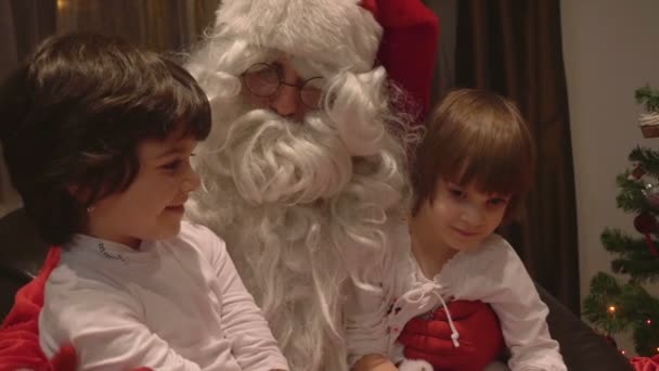 Junge schöne Zwillingsmädchen sitzen am Weihnachtstag im Weihnachtsmann-Schoß - 4k — Stockvideo