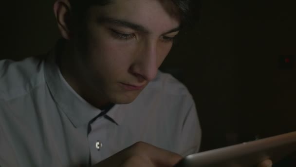 Крупный план молодого красивого мужчины, использующего планшетный компьютер в темноте — стоковое видео