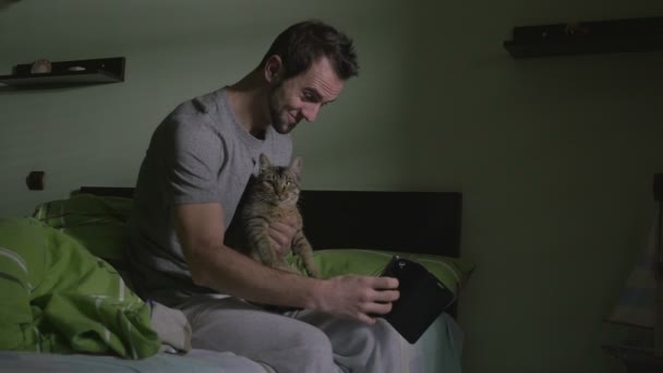 若いハンサムな男はベッドに座って、猫と selfie — ストック動画
