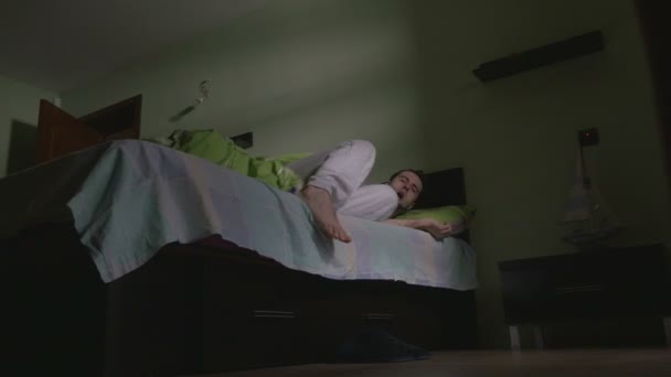 Молодий красивий чоловік прокидається в ліжку і одягає тапочки — стокове відео