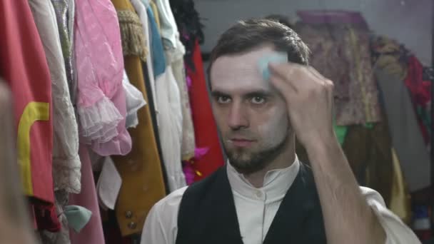 Knappe jonge mannelijke acteur witte gezichtscrème voor MIME-make-up toe te passen — Stockvideo