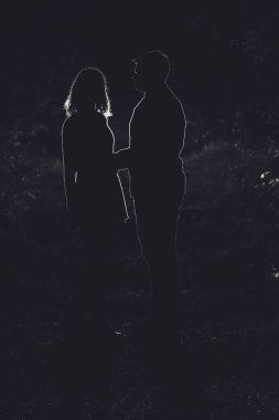 Genç çift gece vakti ormanda eğleniyor. Ormandaki arka ışıklandırmalı çiftin silüeti..