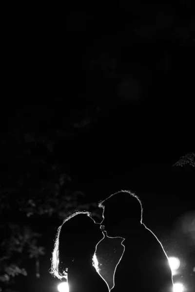 Genç çift gece vakti ormanda eğleniyor. Ormandaki arka ışıklandırmalı çiftin siluet resmi. Öpüşen çift 