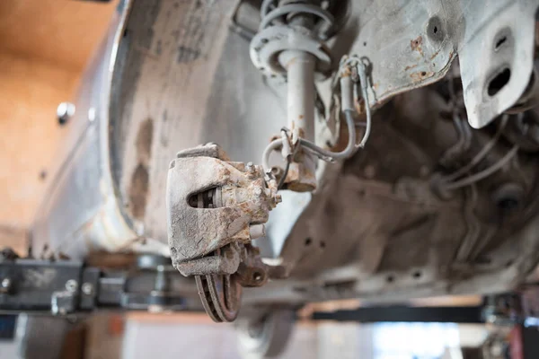 The car lifted on a lift, car suspension covered with rust, brake caliper change.  Auto service industry.