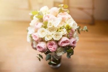 Güneşli bir günde ahşap masada beyaz ve pembe güllerle düğün buketi