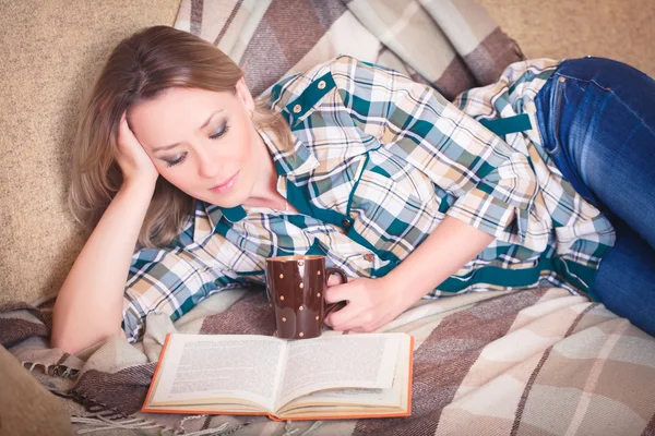 Joven hermosa mujer leyendo tumbado en un sofá —  Fotos de Stock