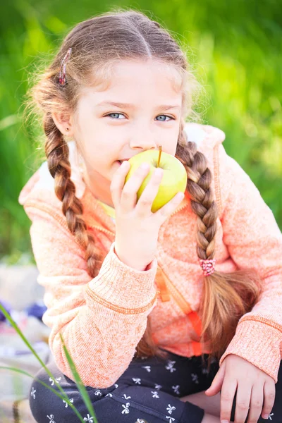 Kleines nettes Mädchen auf grünem Gras mit einem Apfel — Stockfoto