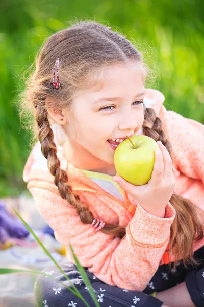 Маленькая милая девочка на фоне зеленой травы с яблоком — стоковое фото