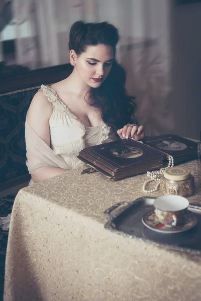 Young woman looks at a photo album. Vintage style, retro interior. — Stock Photo, Image