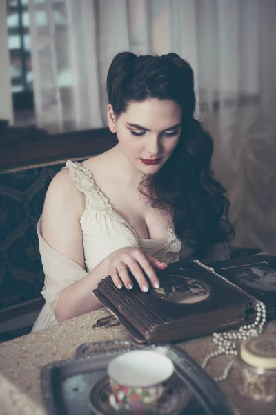 Mujer joven mira un álbum de fotos. Estilo vintage, interior retro. —  Fotos de Stock