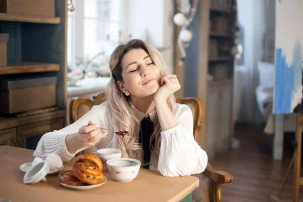 En ung kvinna äter frukost med te och bakverk med sylt. — Stockfoto