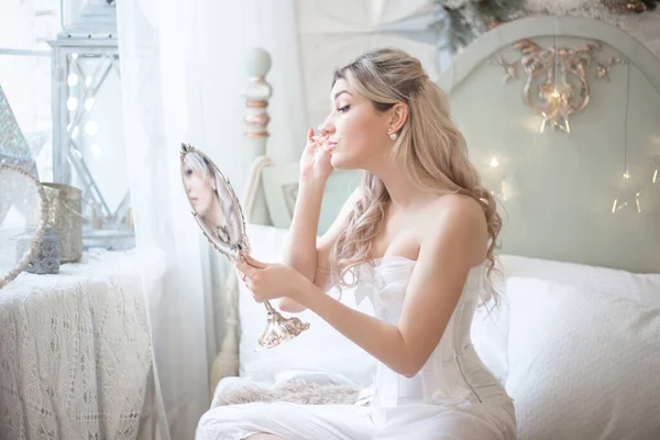 Mooie jonge vrouw in haar slaapkamer met een spiegel. Bruidsmorgen of vintage boudoir. — Stockfoto