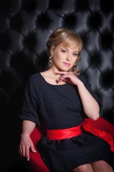 Siyah elbiseli kırmızı bir sandalyede oturan kız — Stok fotoğraf