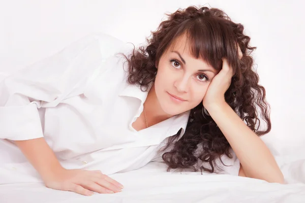 Krásná žena v bílé košili, ležící na posteli — Stock fotografie