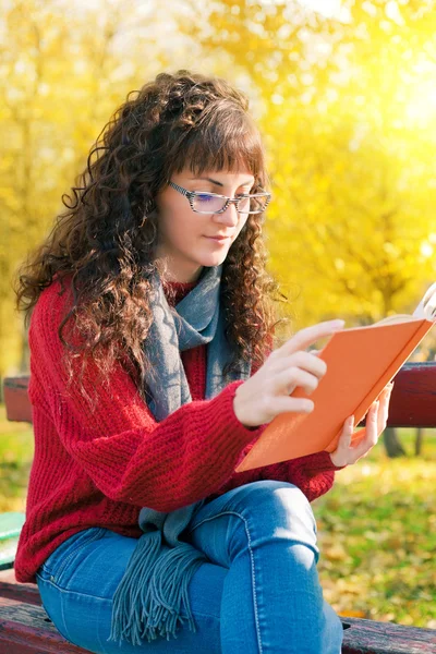 Genç kadın sonbahar Park bir kitap okuma — Stok fotoğraf