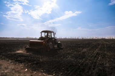 Mavi traktör bahar ekme mevsiminde tohum makinesini çekiyor. Bir traktörle tarım arazisi.