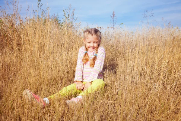 可爱的小女孩坐在草地上，在阳光灿烂的日子 — 图库照片