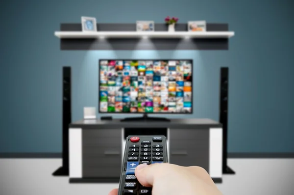 Tittar på TV i moderna TV-rum. Hand som håller fjärrkontrollen — Stockfoto