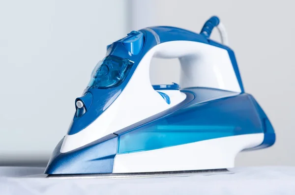 Modern blue steam iron on ironing board — Stock Photo, Image