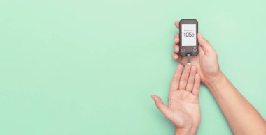 Glukometre kullanan bir adam kan şekeri seviyesini ölçüyor. Fotokopi alanı geniş, yeşil arkaplan. Diyabet kavramı