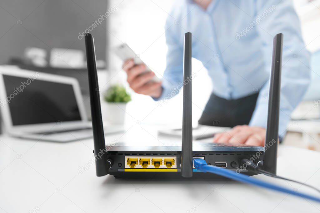 Wireless router with three antennas and cable connected. Man using smartphone in background