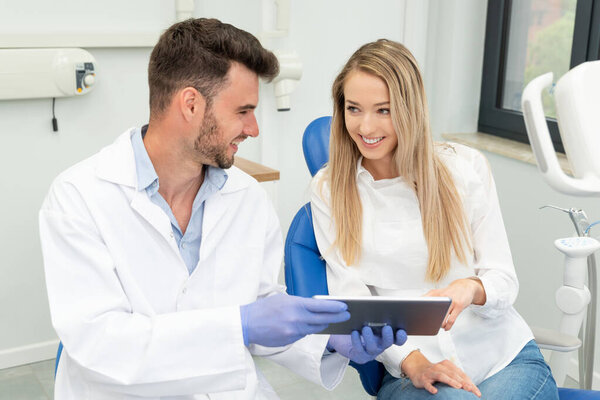 Dental consultation in clinic. Dentist showing teeth x-ray on digital tablet screen