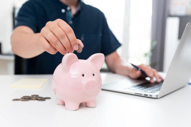 Adam parayı kumbaraya koyar, para biriktirmek için.