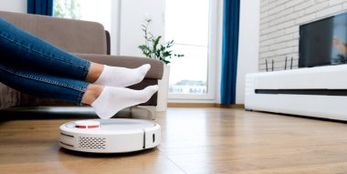 Robot elektrik süpürgesi odayı temizliyor, bacaklar havada. Akıllı ev kavramı